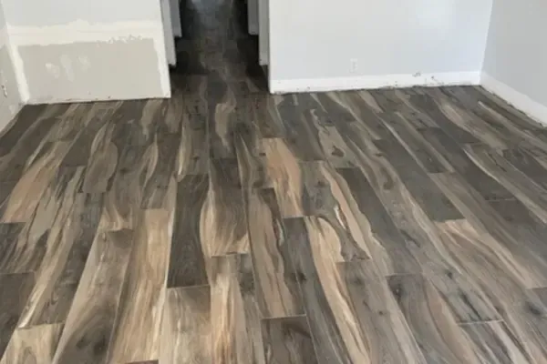 Wide-angle shot of a newly installed wood-look laminate floor in varying shades of gray and tan inside a room.