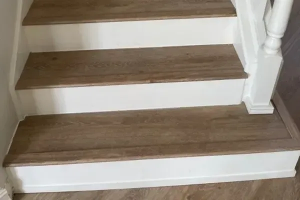 A staircase with three steps featuring light brown wood treads and white risers, ending with a landing at the bottom.