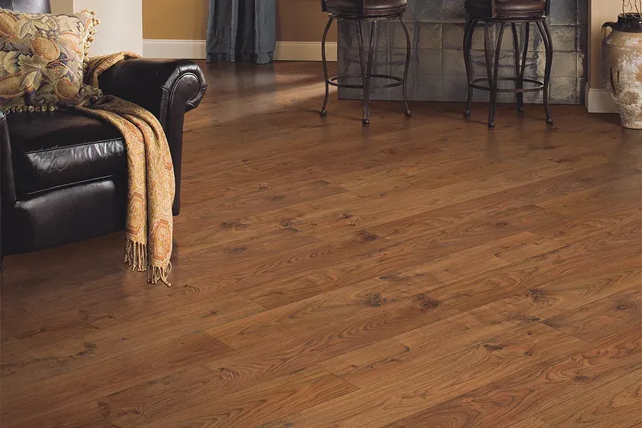 Dark brown hardwood flooring in a room with a leather armchair and a bar area with stools.