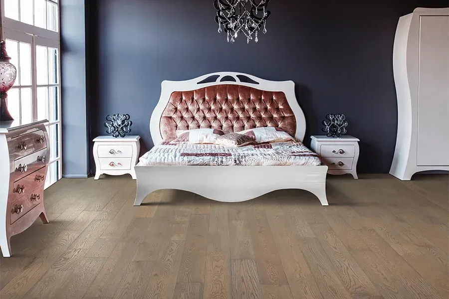A bedroom with a tufted, velvet-upholstered headboard, white wooden furniture, and light brown hardwood flooring.