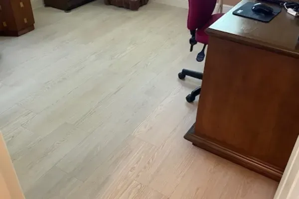 A wooden desk and a red office chair are situated in a room with light-colored wood flooring.