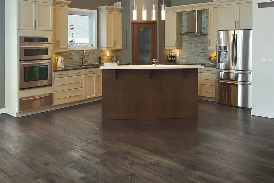 A modern kitchen with cream cabinets, stainless steel appliances, a dark brown island, and dark wood flooring.