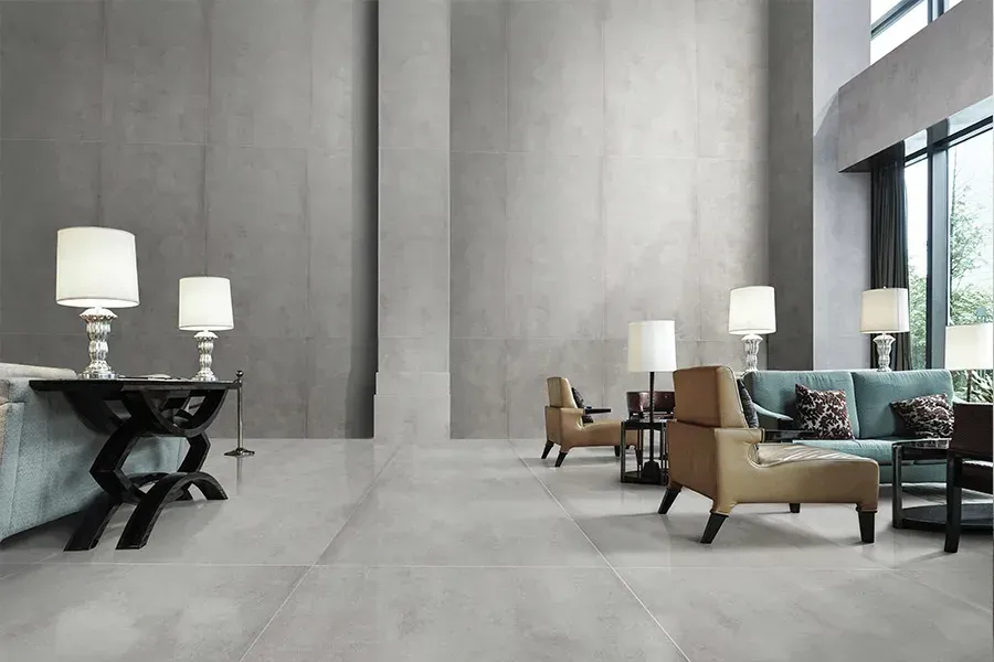 Modern, minimalist lobby with high gray walls, large floor tiles, and beige armchairs arranged in a seating area.