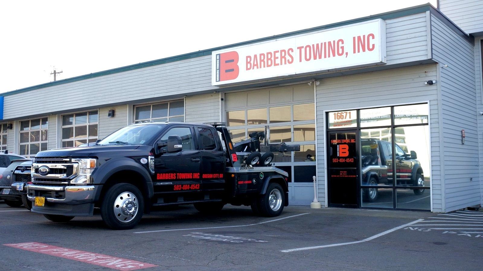 Black tow truck parked outside Barber's Towing, Inc. building. Red and white sign.