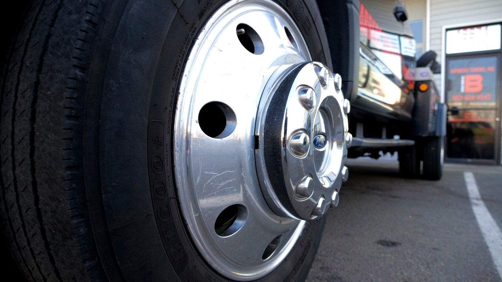 Close-up of a semi-truck wheel; black tire, silver hubcap with circular holes and a chrome center.