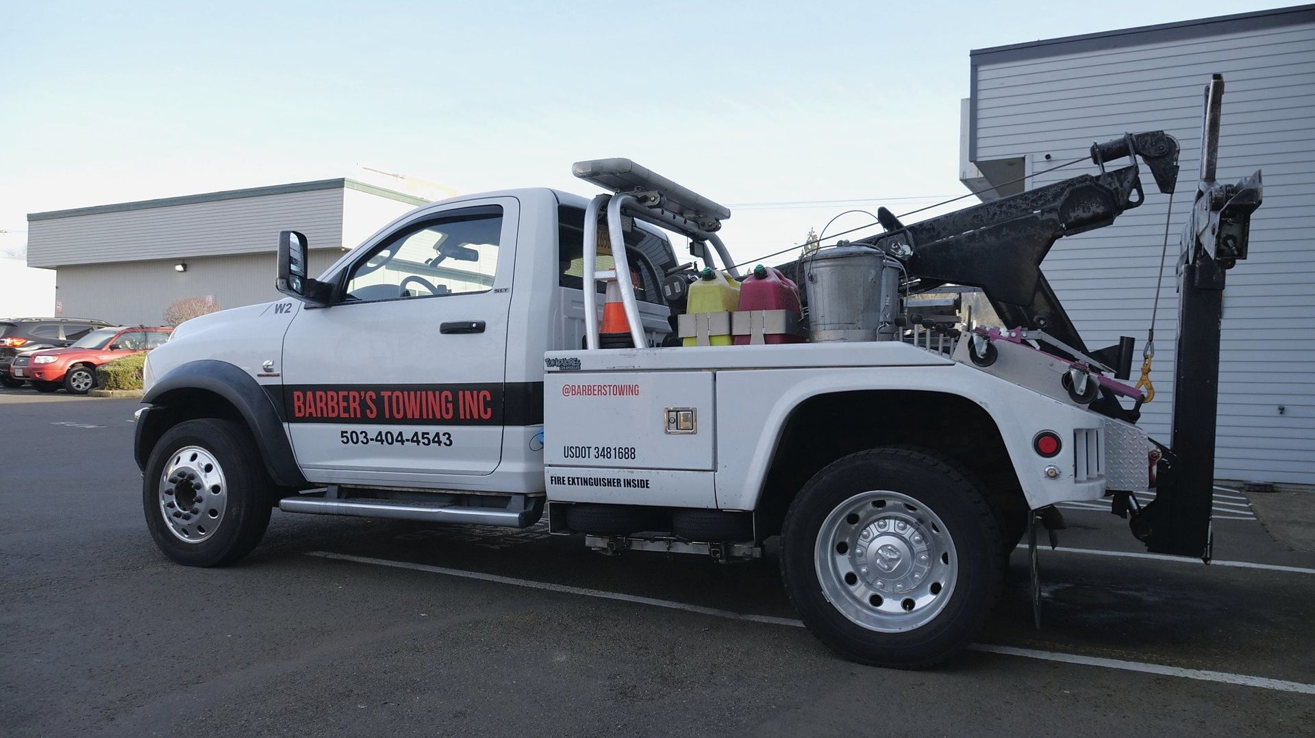 White tow truck parked near a building, with its boom extended. 