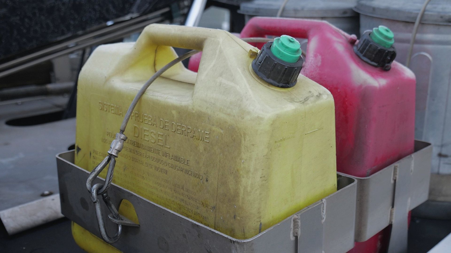 Two gas cans, yellow and red, in a metal rack, outdoor setting.