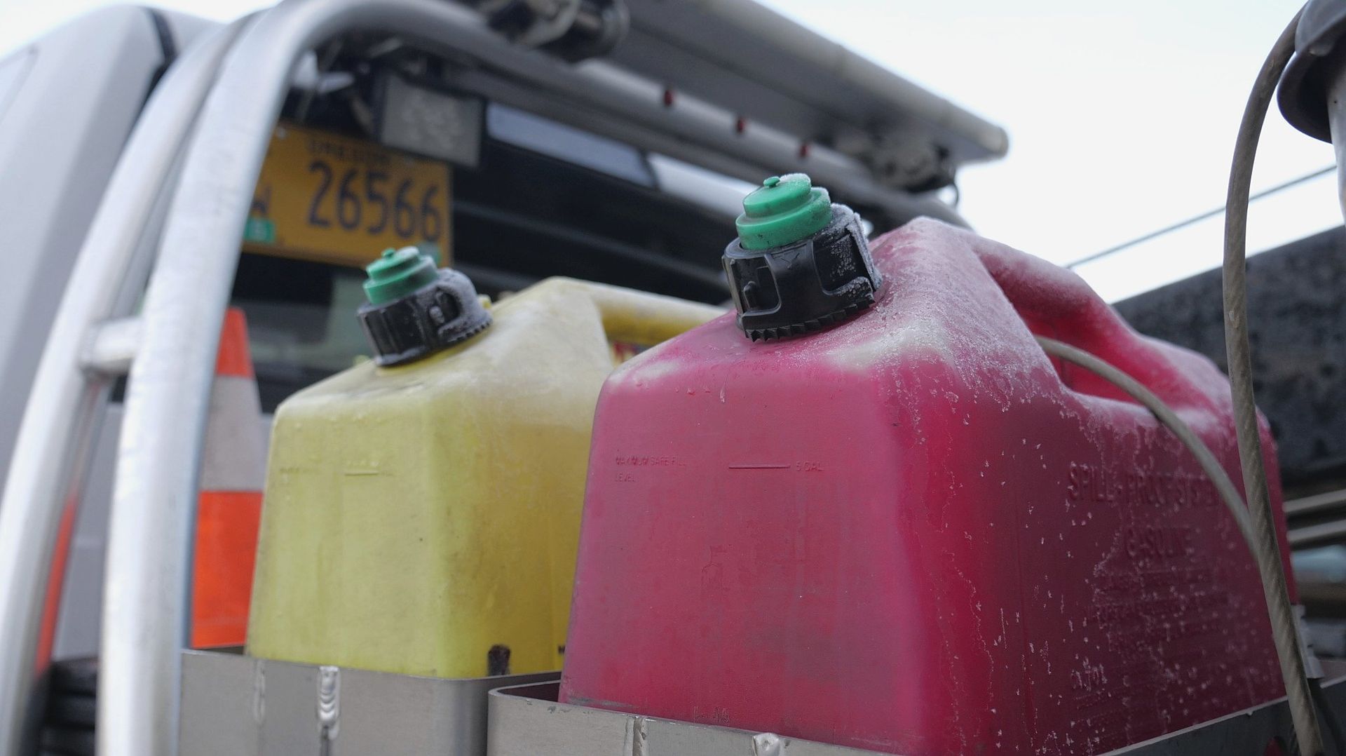 Two gas cans, yellow and red, mounted on a vehicle with a license plate visible.