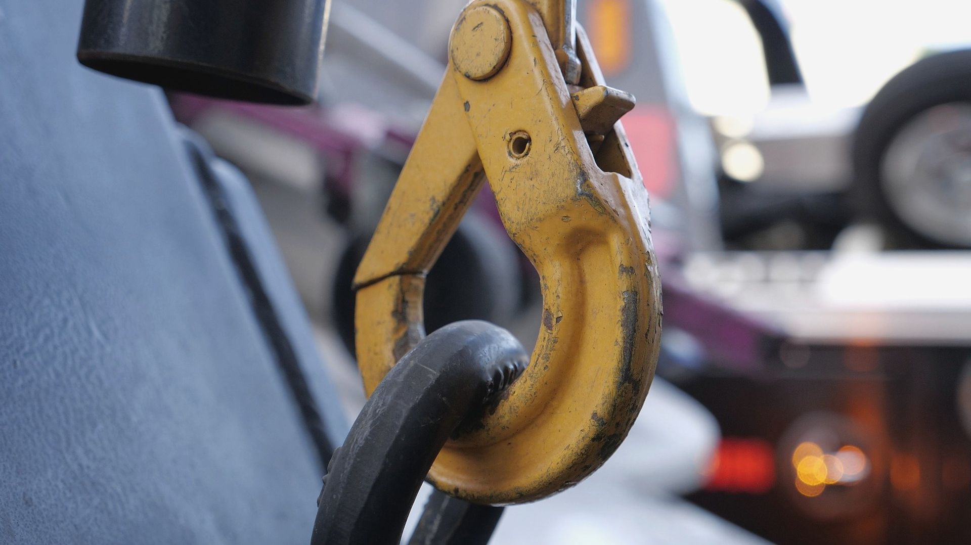Yellow tow hook attached to a black chain, with a blurred vehicle in the background.
