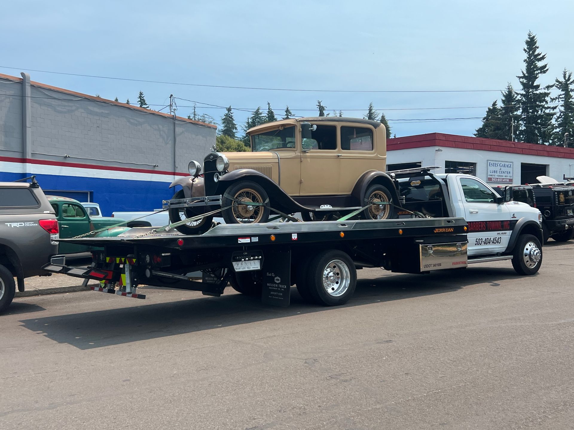A classic tan car loaded on a flatbed tow truck outdoors on a sunny day.