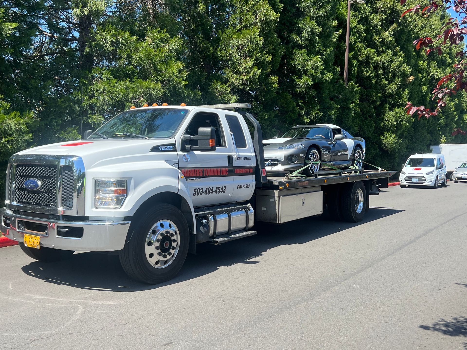 White tow truck hauling a silver sports car on a sunny day.