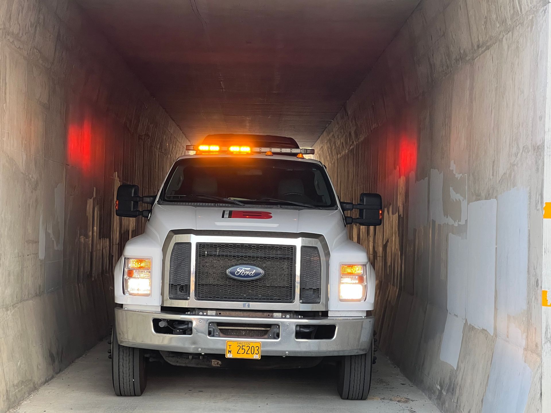 White Ford truck with emergency lights inside a narrow concrete tunnel.
