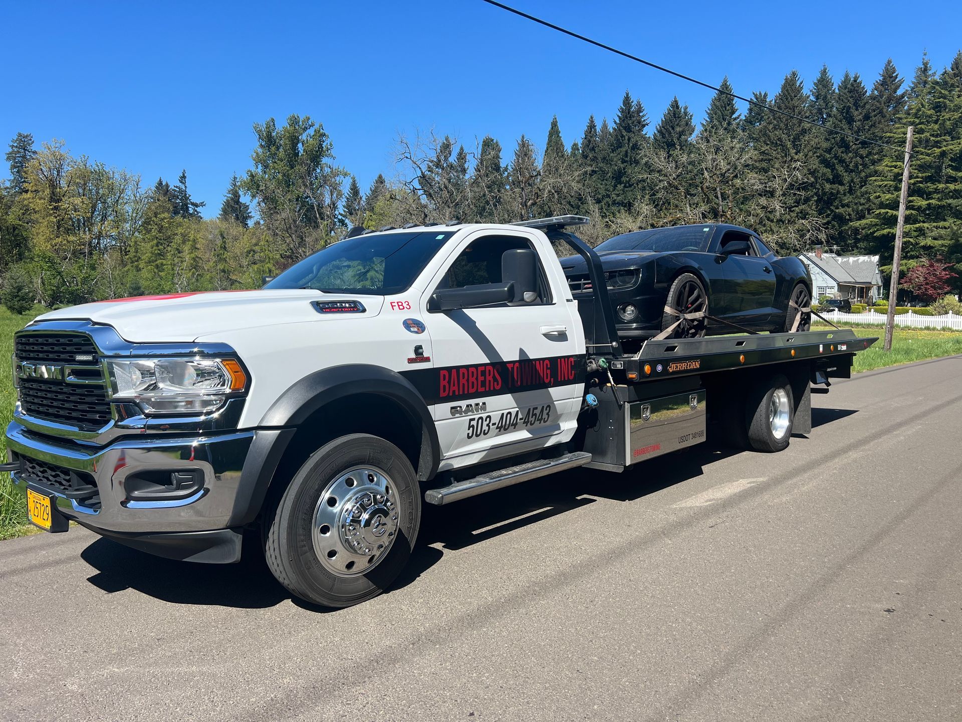 White tow truck hauling a black sports car on a sunny road.