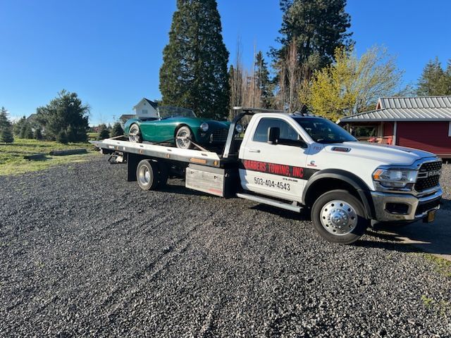 Green sports car on a white tow truck on gravel. Bright, sunny day.