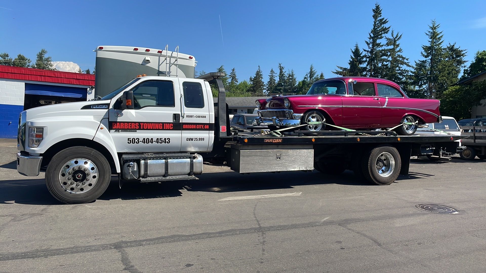 Tow truck hauling a pink classic car. Blue sky, sunny day.