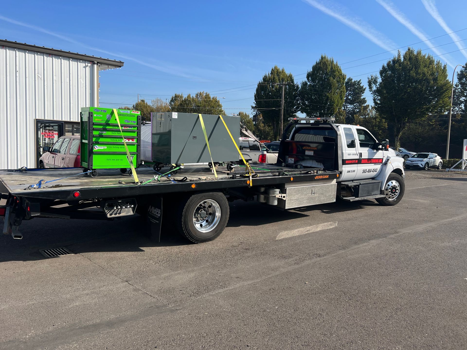 Tow truck hauling equipment on a sunny day. Green and grey boxes secured with yellow straps. 