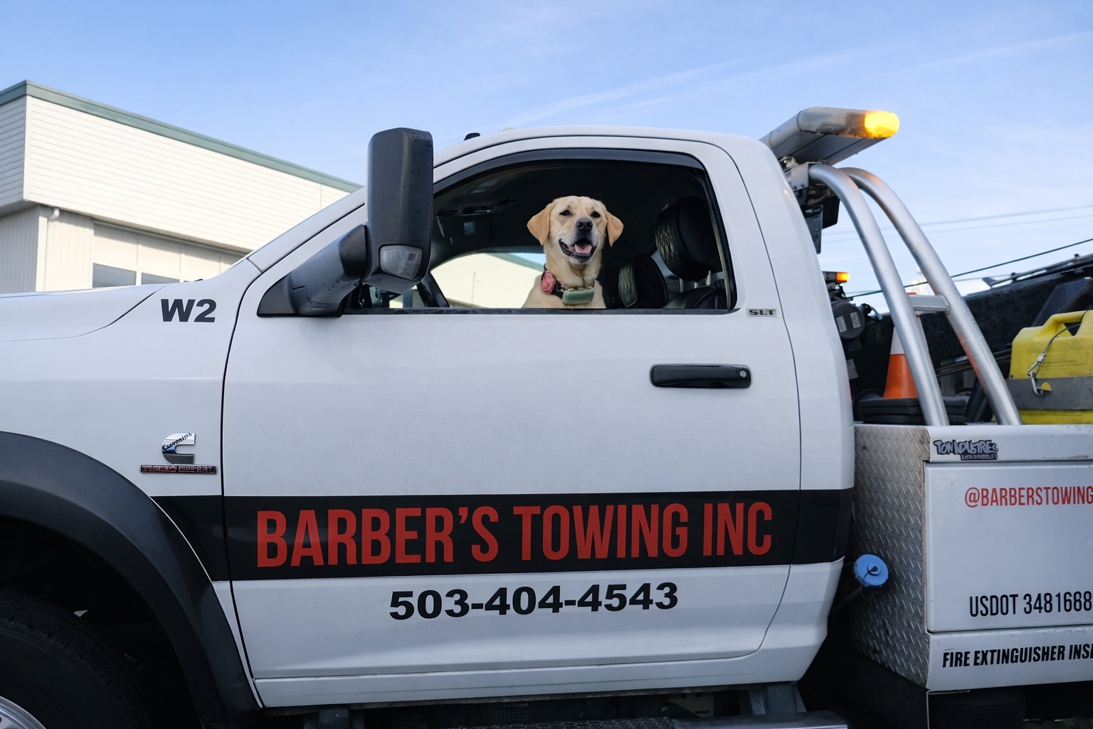 Yellow Labrador dog smiles from the driver's seat of a Barber's Towing truck.