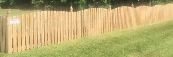 Wooden picket fence running across a sunny grassy yard with a small sign near the left side