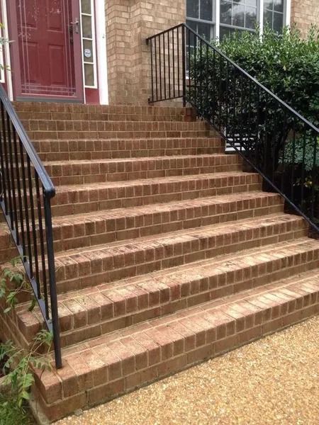 Brick front steps with black railings leading to a red door at a house entrance