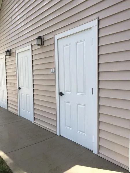 Exterior hallway with two white doors on beige siding and a concrete walkway