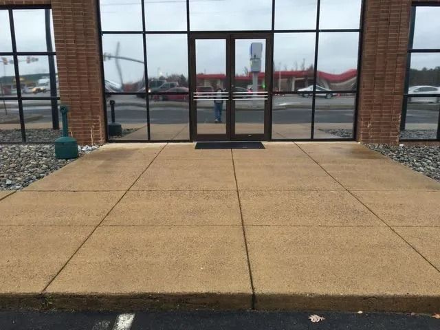 Concrete walkway leading to glass storefront doors under a covered entrance