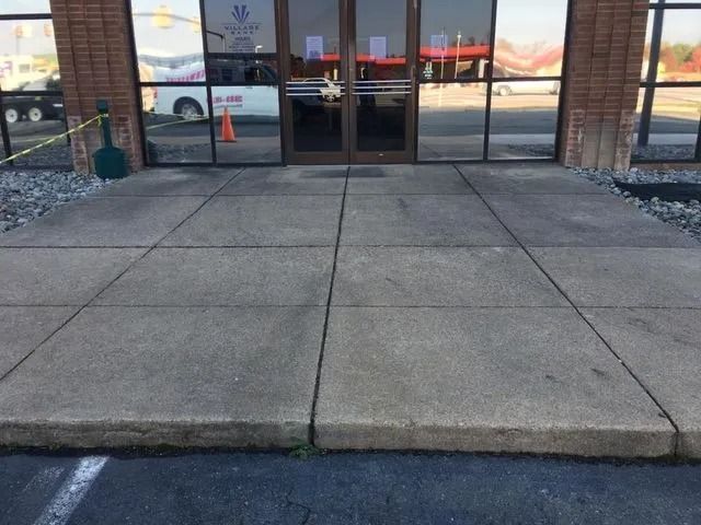 Concrete sidewalk leading to glass storefront doors with brick columns and window reflections