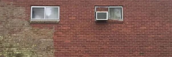 Two small windows set in a red brick wall, one slightly open and one closed.