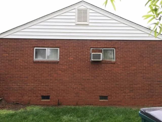 Brick house side wall with two small windows and white gable siding above grass.