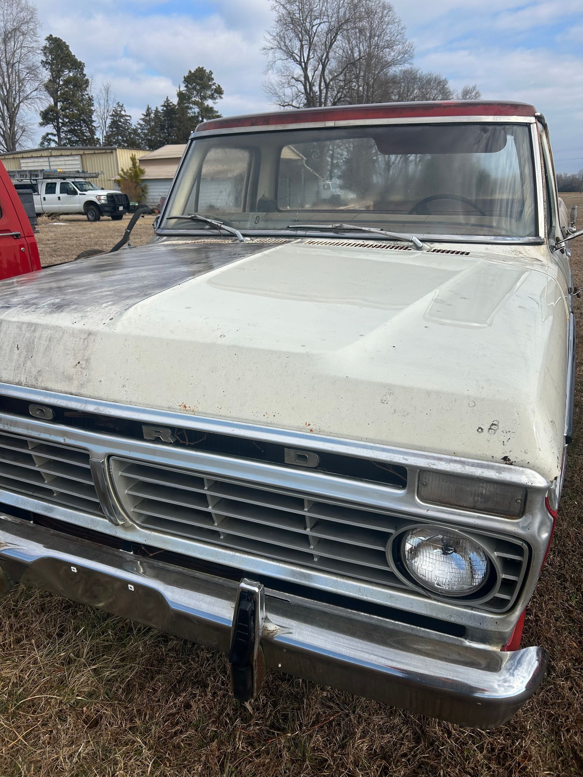 Old white vintage pickup truck with a red cab roof, parked outdoors in a muddy lot.