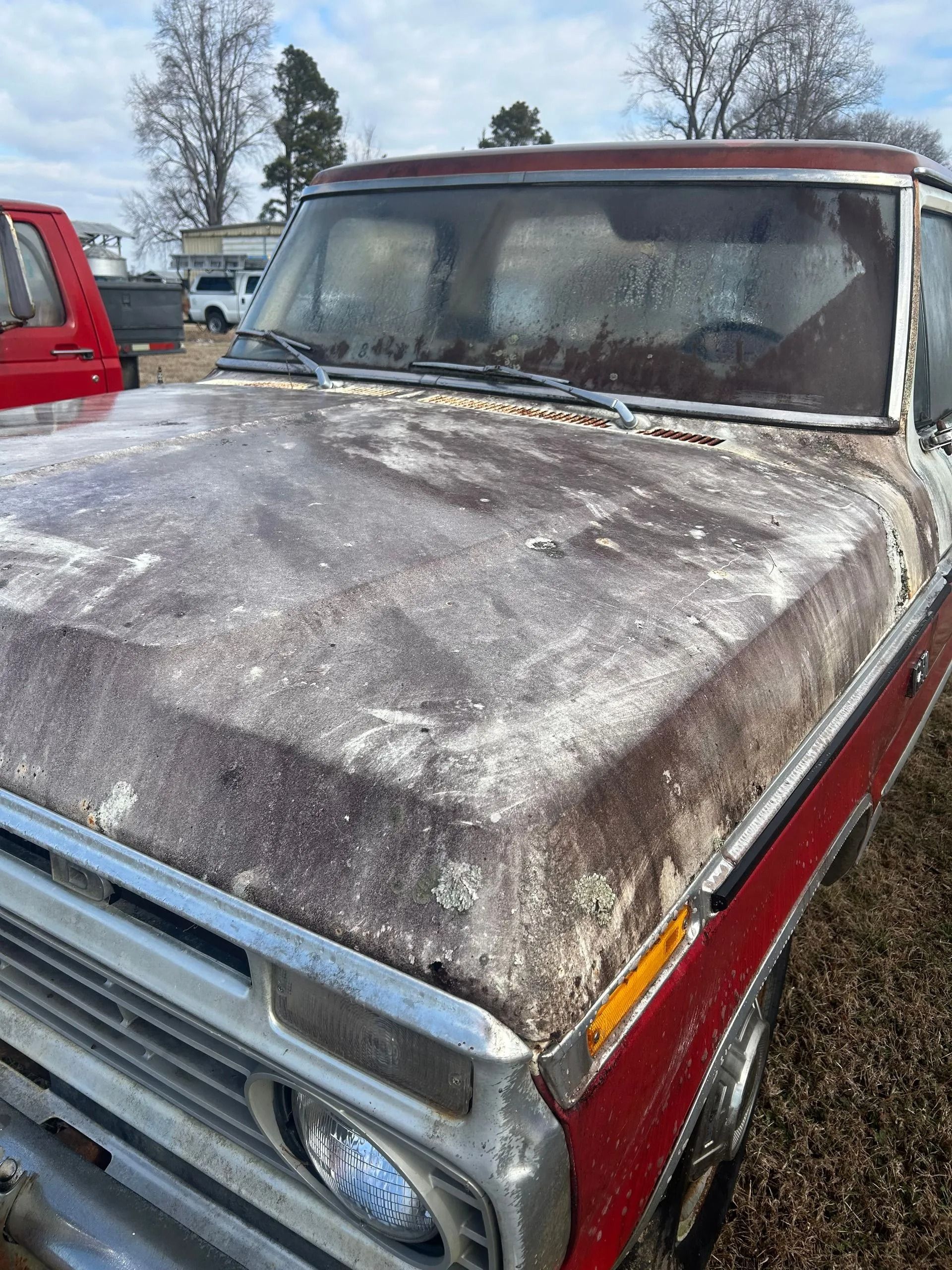 Weathered red pickup truck with a snow- and frost-covered hood parked outdoors