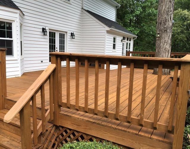 Wooden deck with railings attached to a white house, overlooking trees and a wooded yard