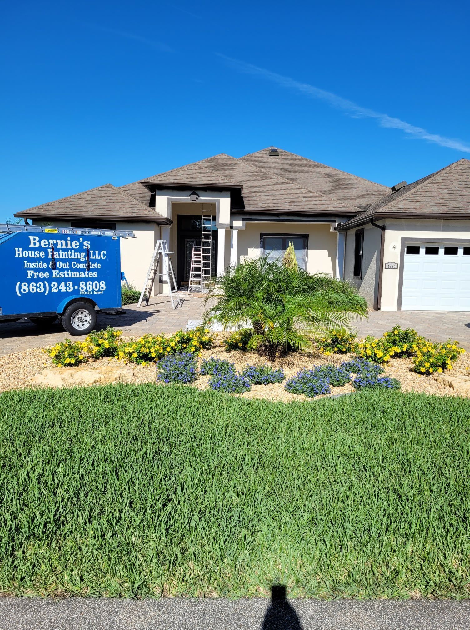 A light beige house with a brown roof and a green lawn under a bright blue sky. A work truck is parked out front.