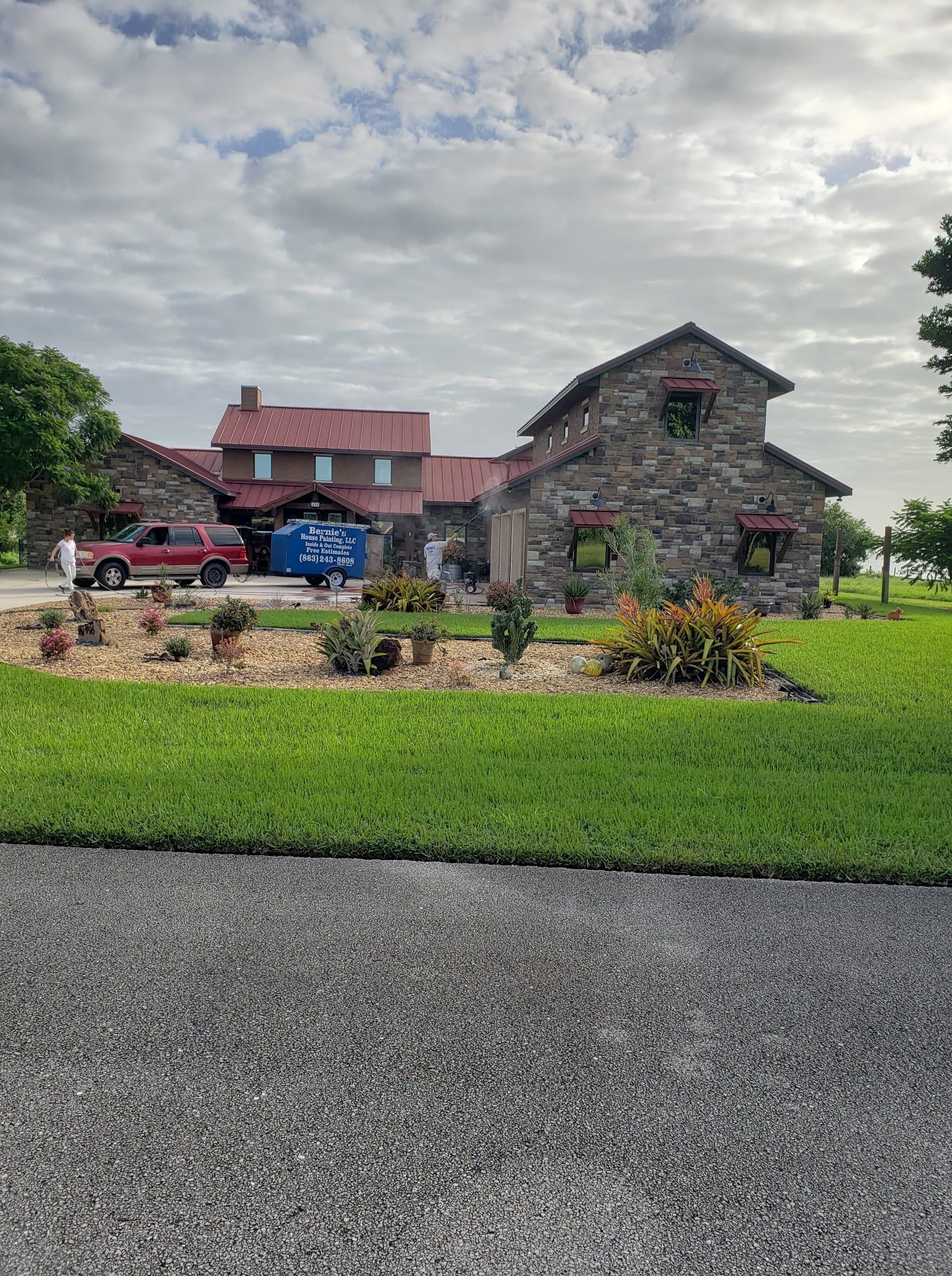 Stone building with red roof, truck parked in front, cloudy sky.