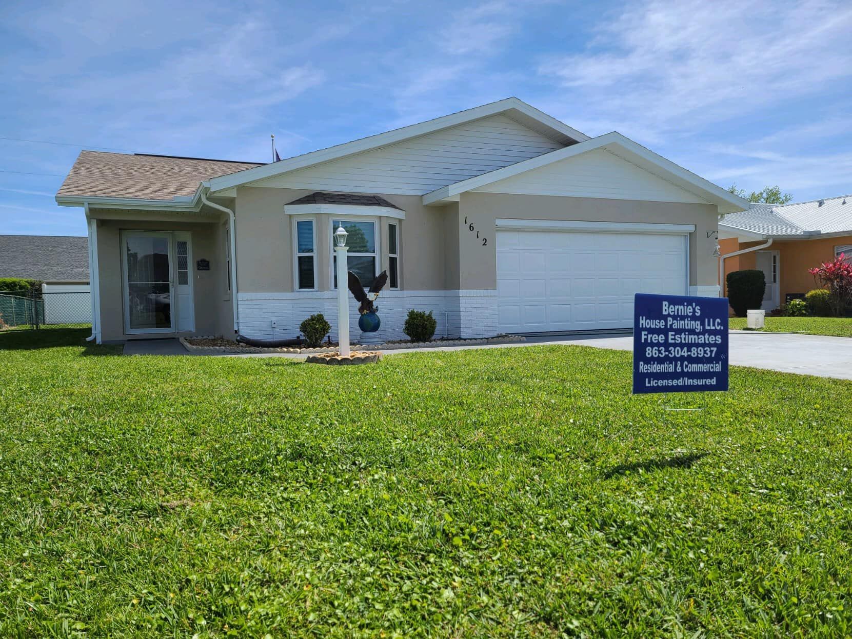 Tan house with a white garage door, a lawn, and a for-sale sign.