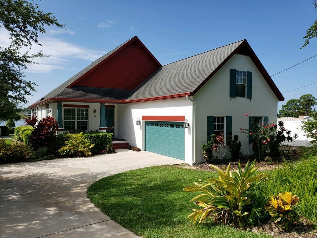 White house with red accents, teal garage door, and shutters. Green lawn and driveway.