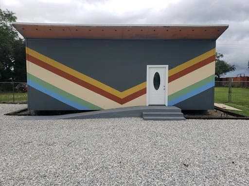 Gray building with angled stripes, a white door, ramp, and steps.