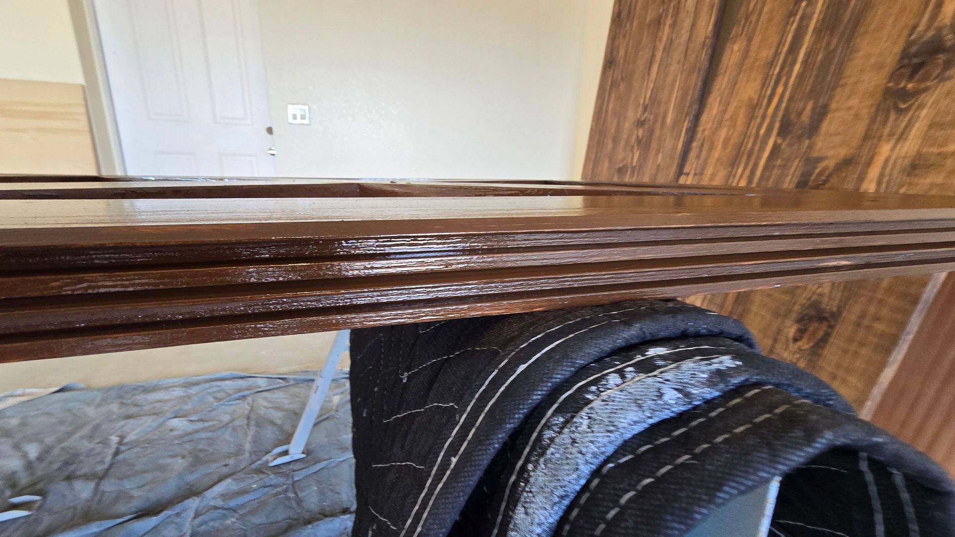 Dark brown wood planks stacked on a sawhorse, close-up with a moving blanket.