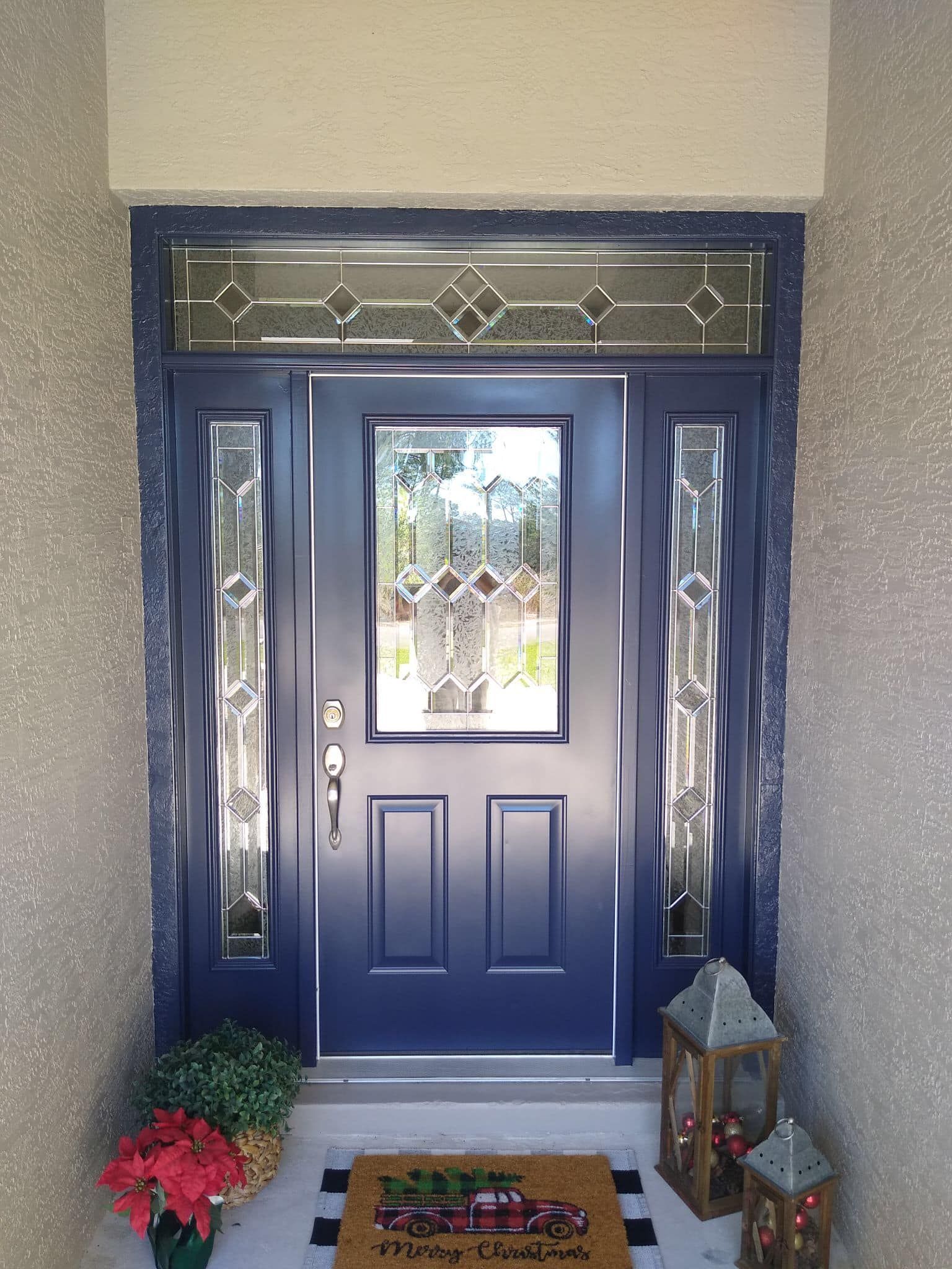 Blue front door with glass panels and a transom window, decorated with holiday accents.