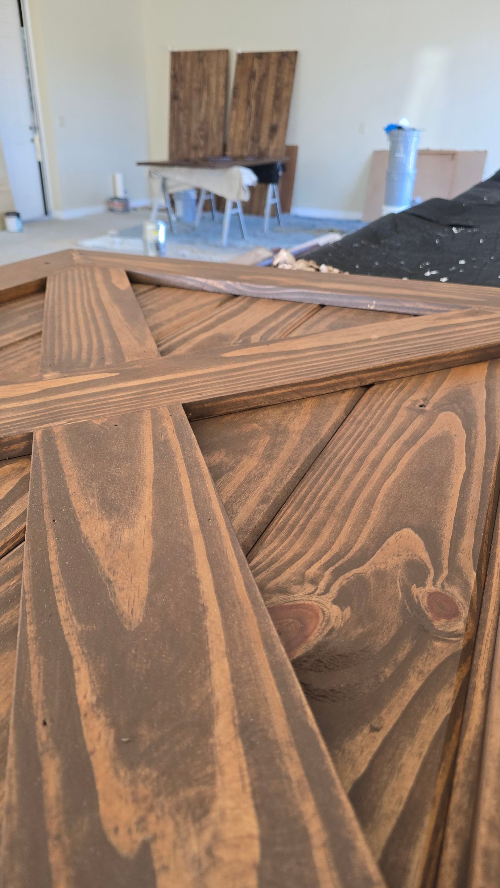 Close-up of a stained wooden barn door with an X-shaped brace; construction site background.