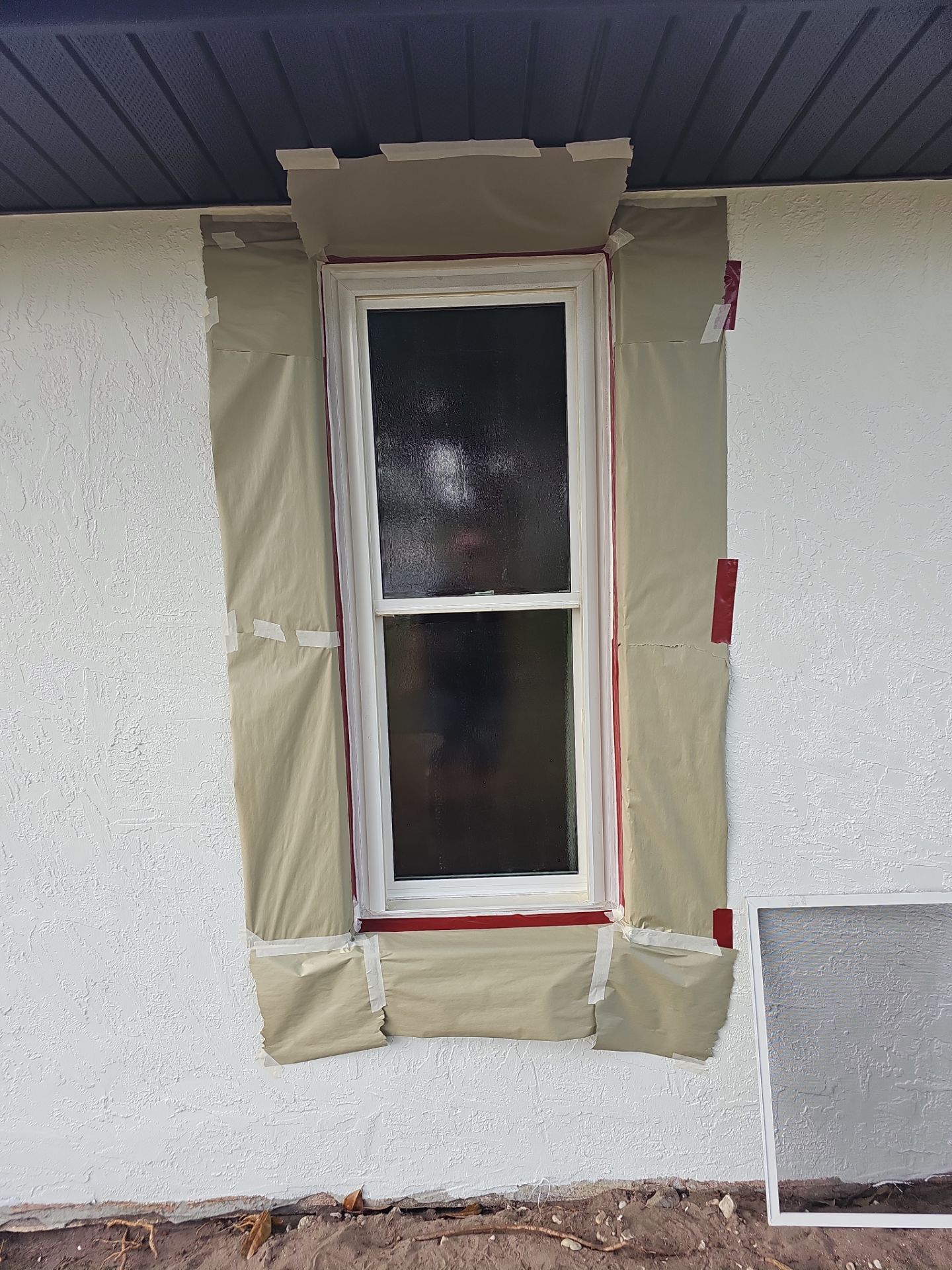 Window taped for painting, on a textured white exterior wall.