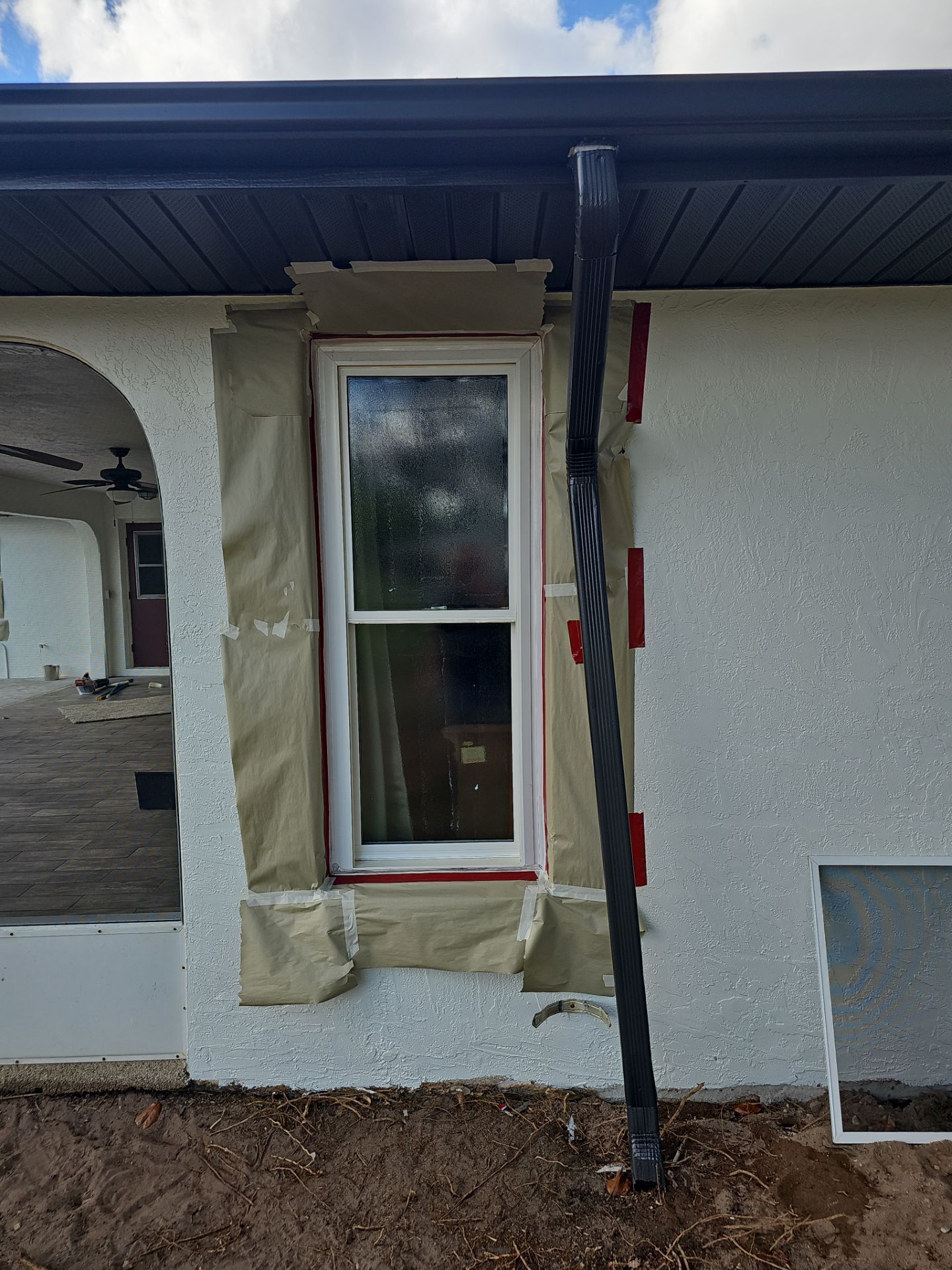A white window on a stucco wall, wrapped in paper, with a black gutter and red shims.