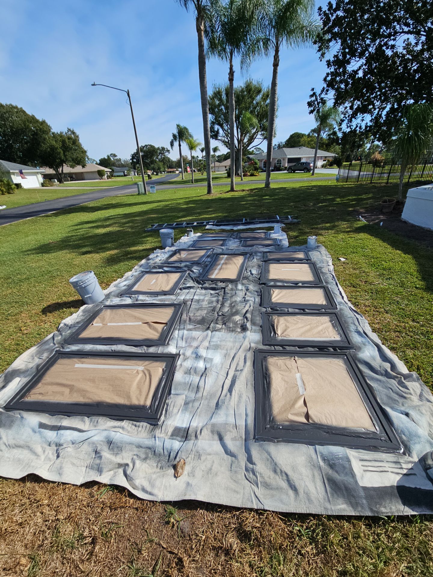 Painted window frames on a tarp in a grassy yard, under a sunny sky.
