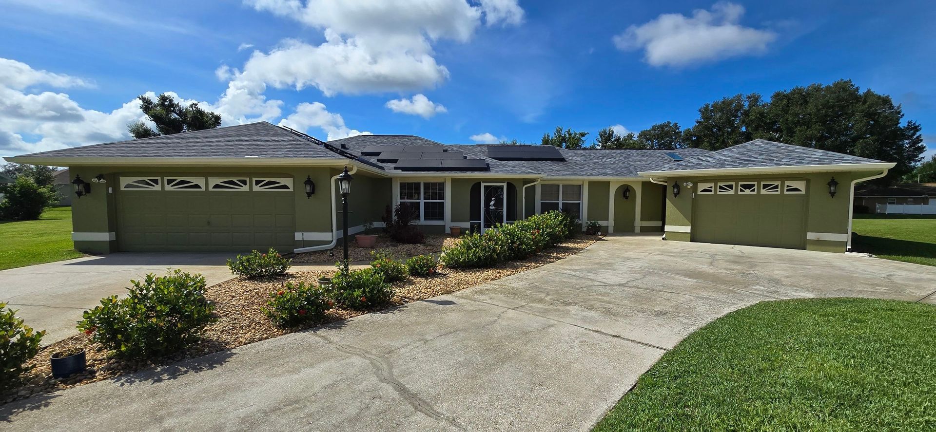 A light green house with a dark roof and a long driveway on a sunny day.