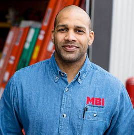 Man in blue denim shirt with MBI logo, standing in front of shelves with red binders
