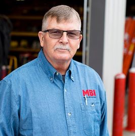 Man in blue button-up shirt and glasses stands in a workshop doorway