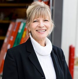 Smiling woman in a black blazer and white turtleneck standing in front of colorful bookshelves