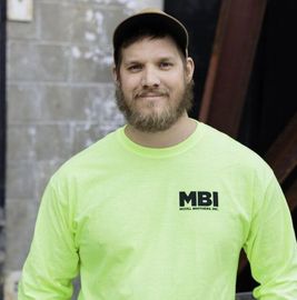 Man in neon green MBI shirt and cap standing indoors against a concrete wall
