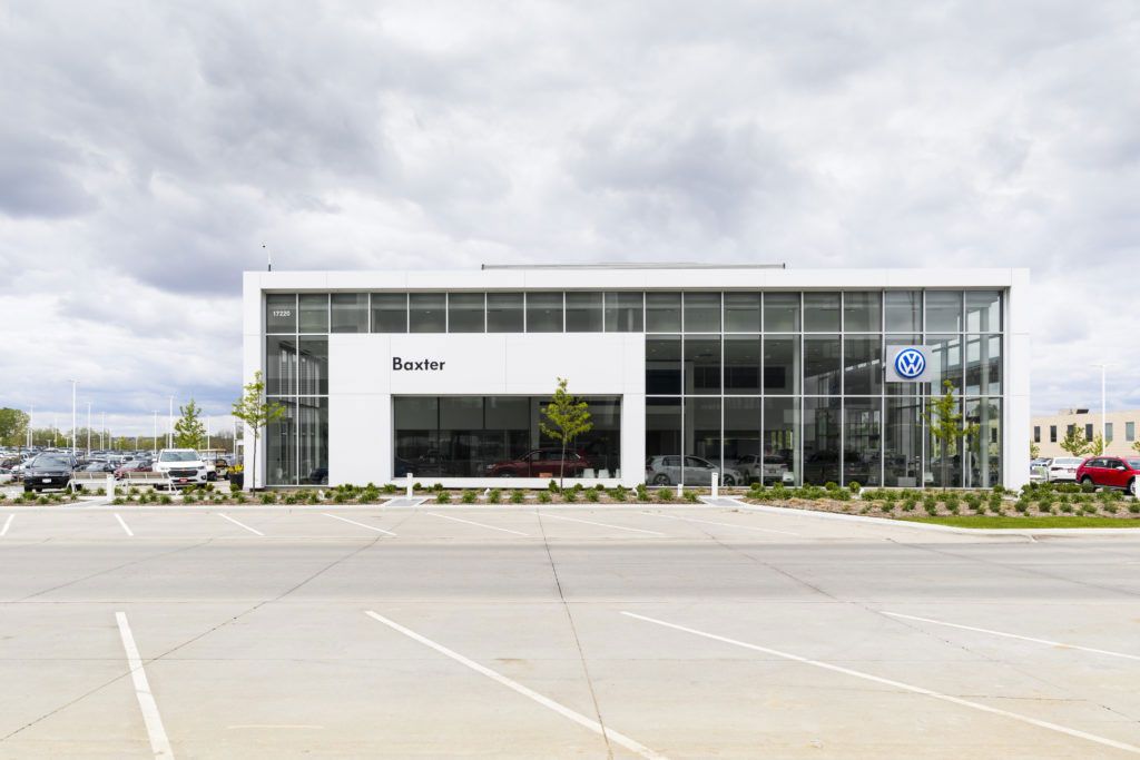 Modern glass-front office building with a white entrance, cloudy sky, and empty parking lot