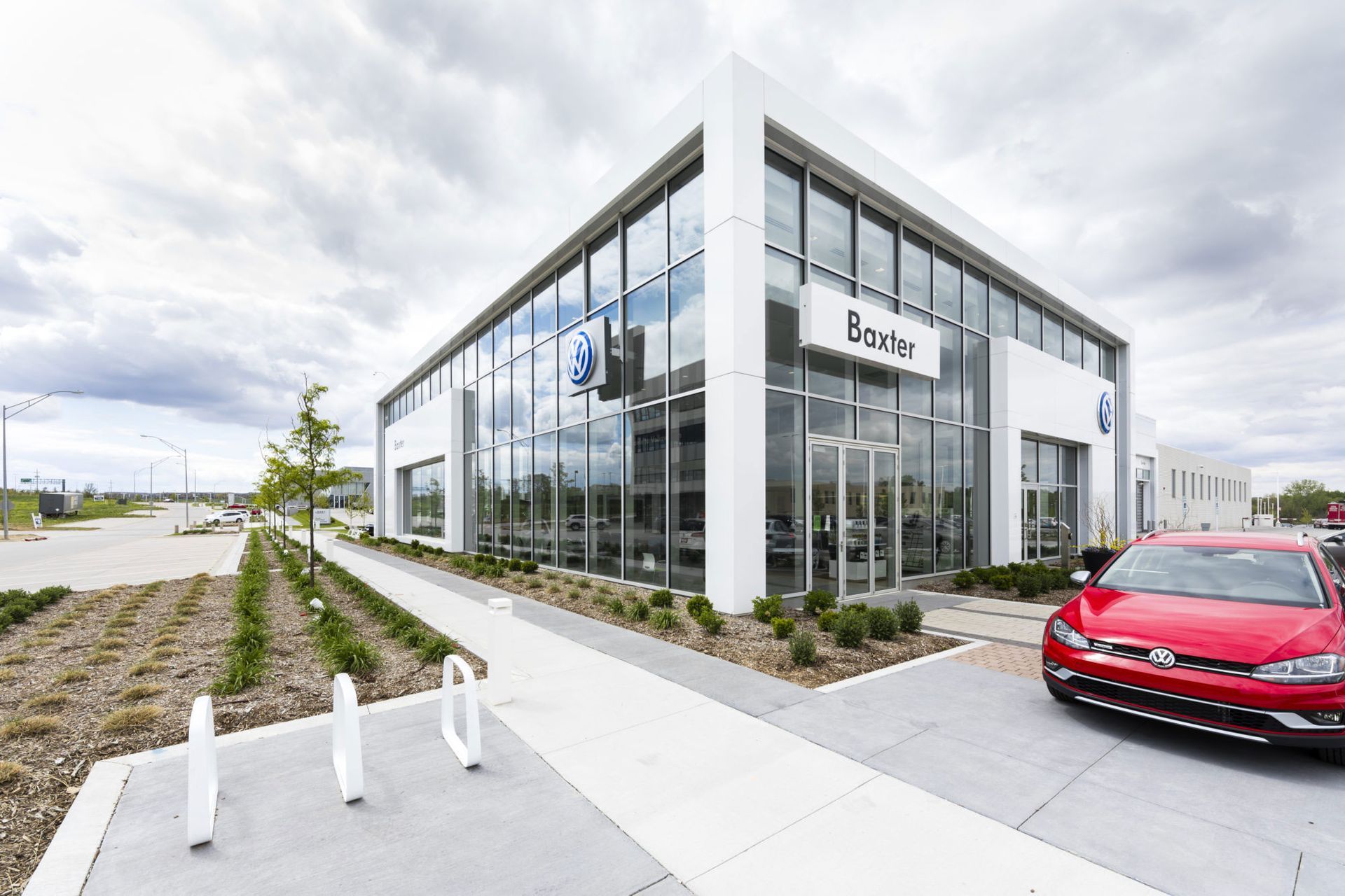 Modern glass office building with landscaped walkway and a red car parked outside