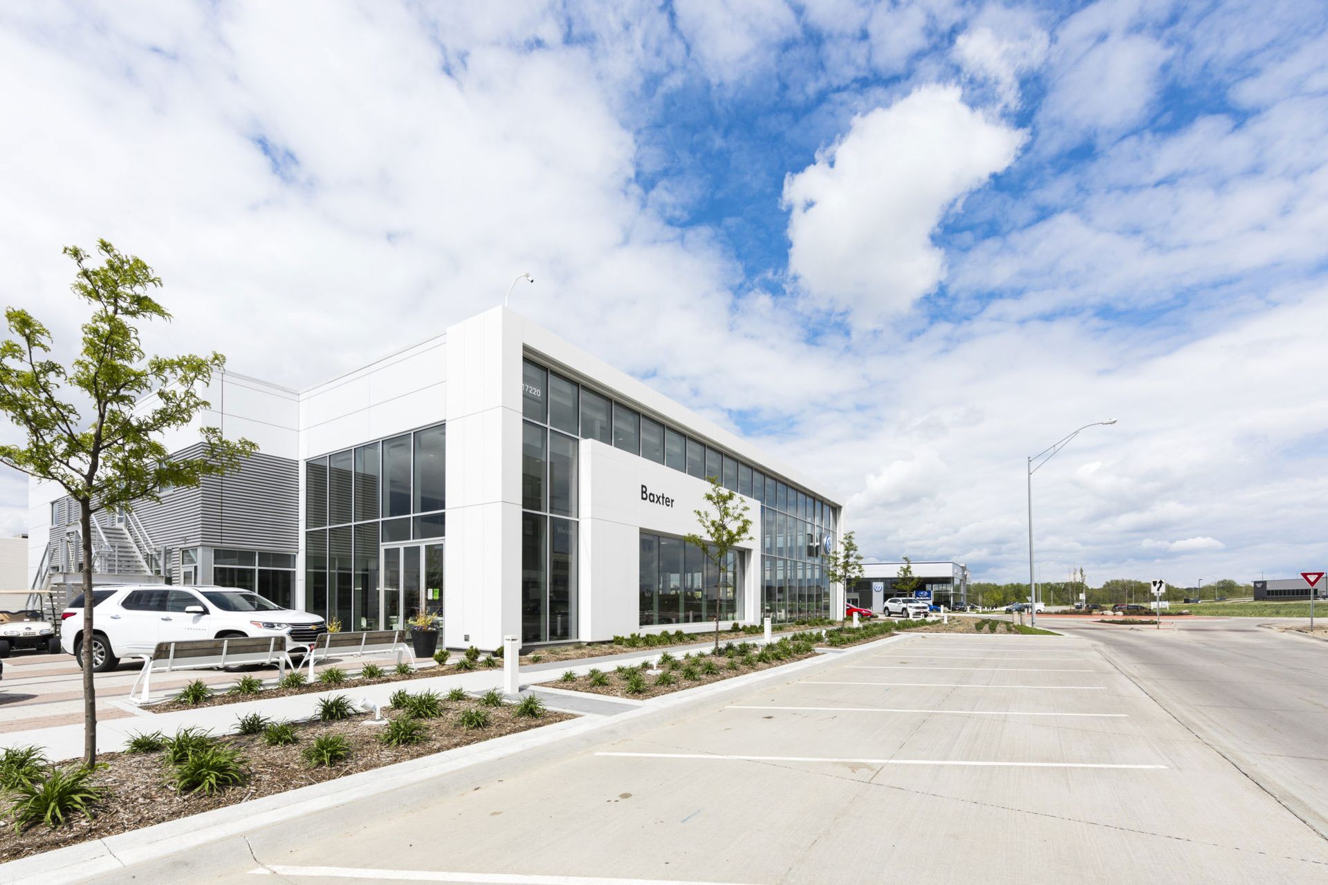 Modern office building with glass facade beside an empty parking lot under a partly cloudy sky